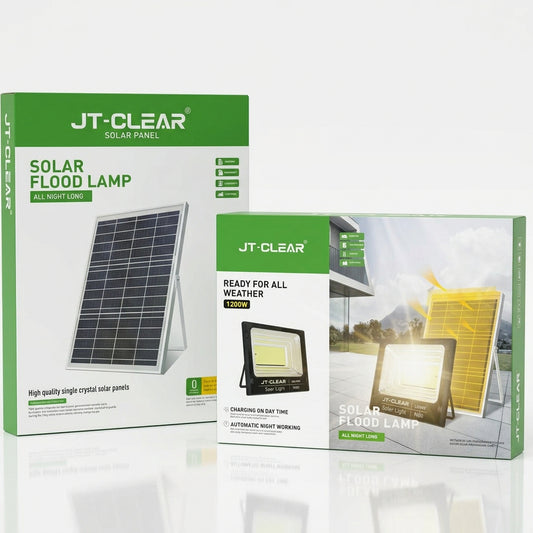 Two JT-CLEAR solar product boxes displayed on a dark reflective surface with dramatic light rays behind them. The larger box reads 'SOLAR FLOOD LAMP' and the smaller box reads 'READY FOR ALL WEATHER.